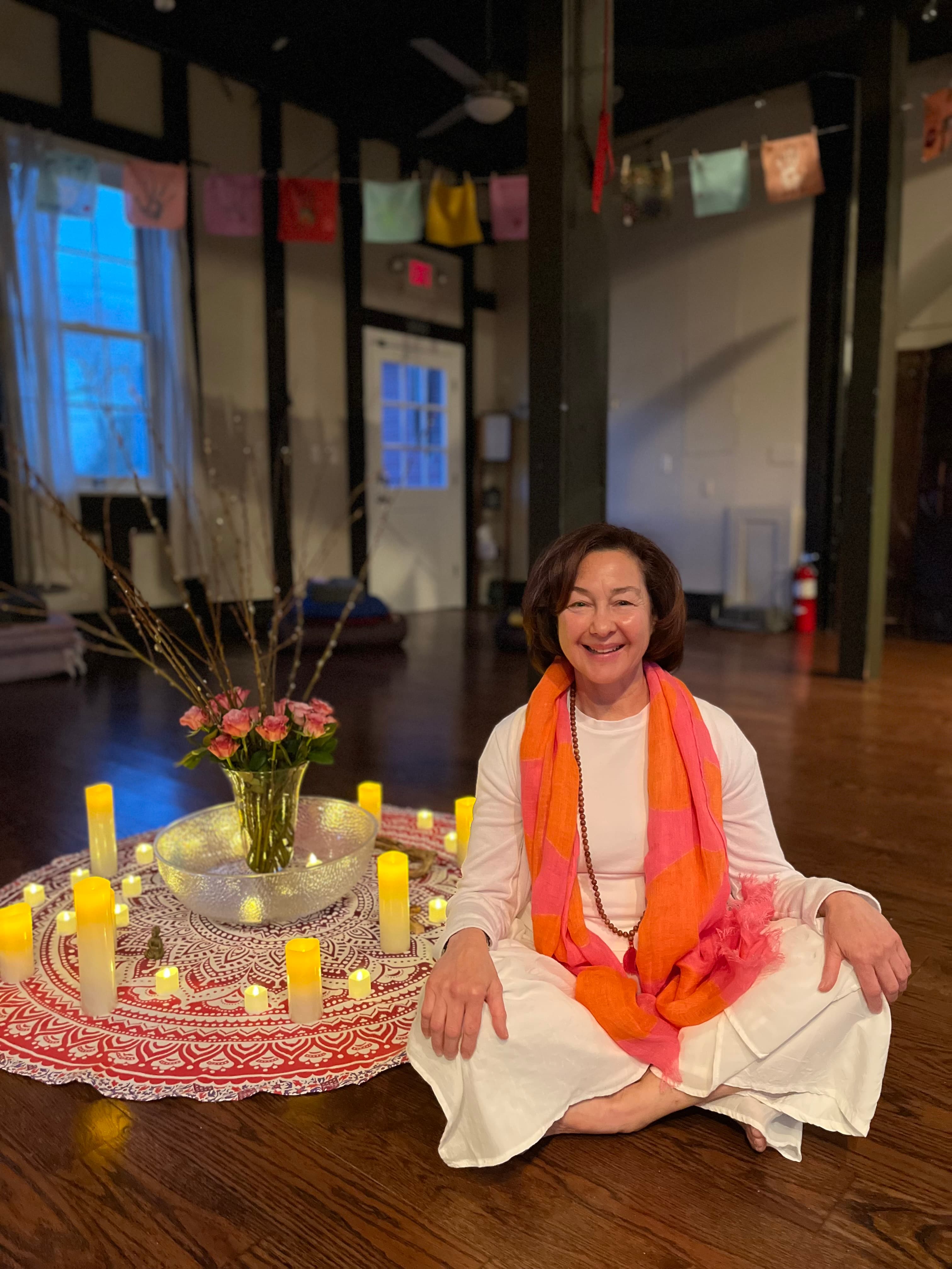 Cynthia Tarantino seated in meditation with candles and flowers in a warm studio